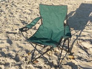 Das Bild zeigt einen faltbaren Beachstuhl im Sand.