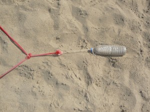 Auf dem Bild sieht man eine mit Sand gefüllte Plastikflasche die als improvisierte Befestigung für die Linien des Beachvolleyballfeldes dient.