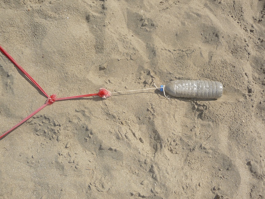 Auf dem Bild sieht man eine mit Sand gefüllte Plastikflasche die als improvisierte Befestigung für die Linien des Beachvolleyballfeldes dient.