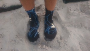 Auf dem Bild sieht man 2 Füße im Sand, welche Vincere Beachsocken zum Schutz vor Kälte tragen.