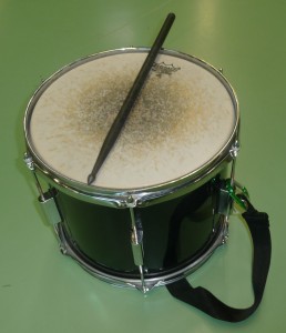 Das Bild zeigt eine schwarze Fantrommel (12") mit Remo-Schlagfell und einen Drumstick aus Carbon