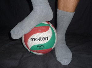 Das Bild zeigt einen Volleyball und 2 Füße in grauen Socken.