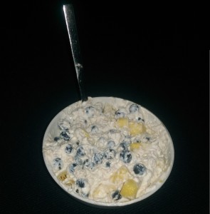 Das Bild zeigt eine weiße Schüssel mit dem das Fitness-Frühstück bestehend aus Speisequark, Milch, Haferflocken, Blaubeeren und Ananas.