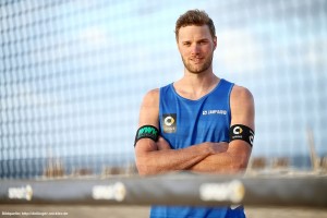 Das Foto zeigt Beachvolleyballer Armin Dollinger mit verschränkten Armen hinter einem Beachvolleyballnetz am Strand