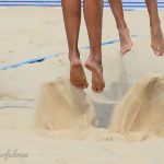 4 Füße von 2 Beacherinnen beim Absprung im Sand auf dem Beachvolleyballfeld