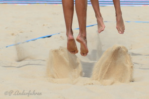 4 Füße von 2 Beacherinnen beim Absprung im Sand auf dem Beachvolleyballfeld