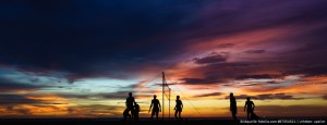 Das Bild zeigt Beachvolleyballer am Strand vorm Sonnenuntergang, die Volleyball spielen