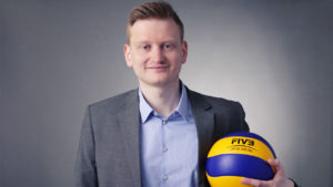 Das Foto zeigt Social Media-Verantwortlicher des DVV: Lars Gäbler im grauen Anzug und blauen Hemd. In der linken Hand hält er einen blau gelben Mikasa Volleyball MVA 300.