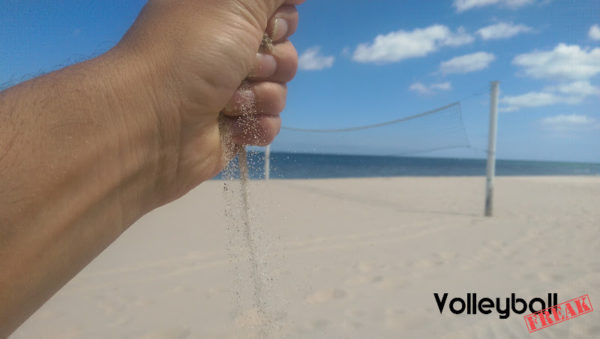 Das Foto zeigt eine Hand voll Sand, welcher aus ihr herausrieselt. Dies steht für die Durchlässigkeit. Im Hintergrund ist ein Beachvolleyballnetz zu sehen.