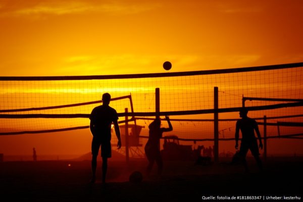 Das Foto zeigt 3 Beachvolleyballer beim Spielen im Sonnenuntergang am Strand.