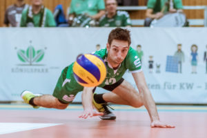 Daniel Heinecke versucht den blau-gelben Mikasa Volleyball noch abzuwehren indem er seine flache Hand zwischen Ball und Boden schiebt.