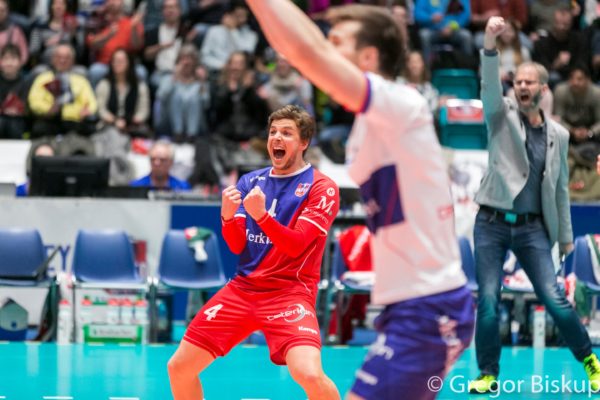 United Volleys Spieler Patrick Steuerwald (rot-blaues Trikot) jubelt über den Punkt. Im Vordergrund sieht man unscharf Julian Zenger und im Hintergrund Michael Warm.