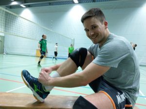 Das Foto zeigt Volleyballfreaktester Manu mit den Mizuno Wave Tornado X2 auf einer Bank. Im Hintergrund läuft das Training.