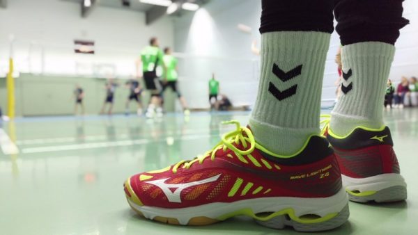 Das Foto zeigt die roten Mizuno Wave Lightning Z4 Volleyballschuhe im Vordergrund. Im Hintergrund findet ein Volleyballspiel statt.