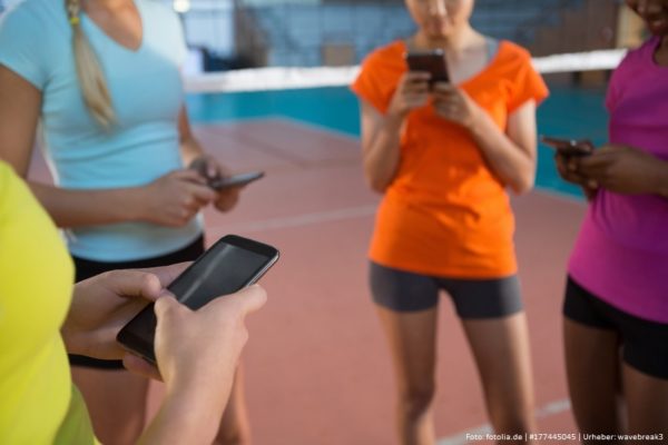 Teenager stehen vor einem Volleyballnetz und schauen auf ihr Smartphone