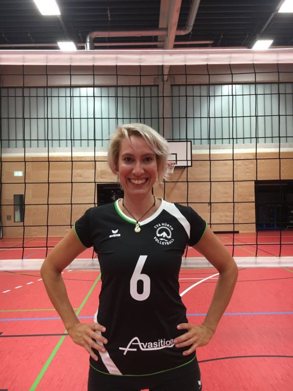 Portraitfoto einer Volleyballspielerin vor einem Netz. Aber mit dem Makel eines offenen Garagentor im Hintergrund.