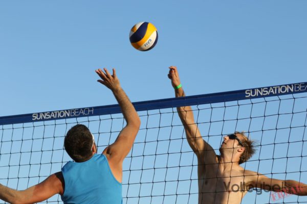 Das Foto zeigt 2 Beachvolleyballspieler im Luftduell am Beachvolleyballnetz.