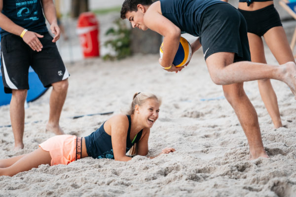 Das Foto zeigt eine Beachvolleyballspielerin lachend am Boden liegend. 